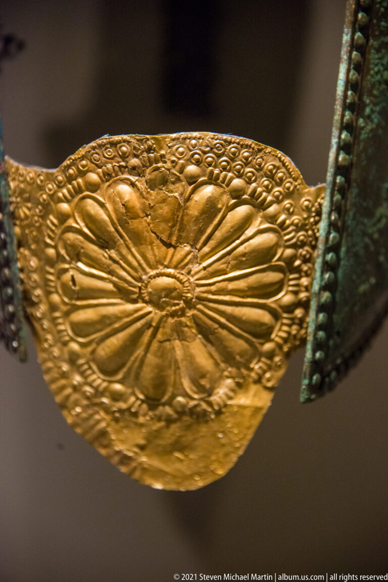 Close view of an embossed gold plaque with a large radiating floral motif and stippled border.