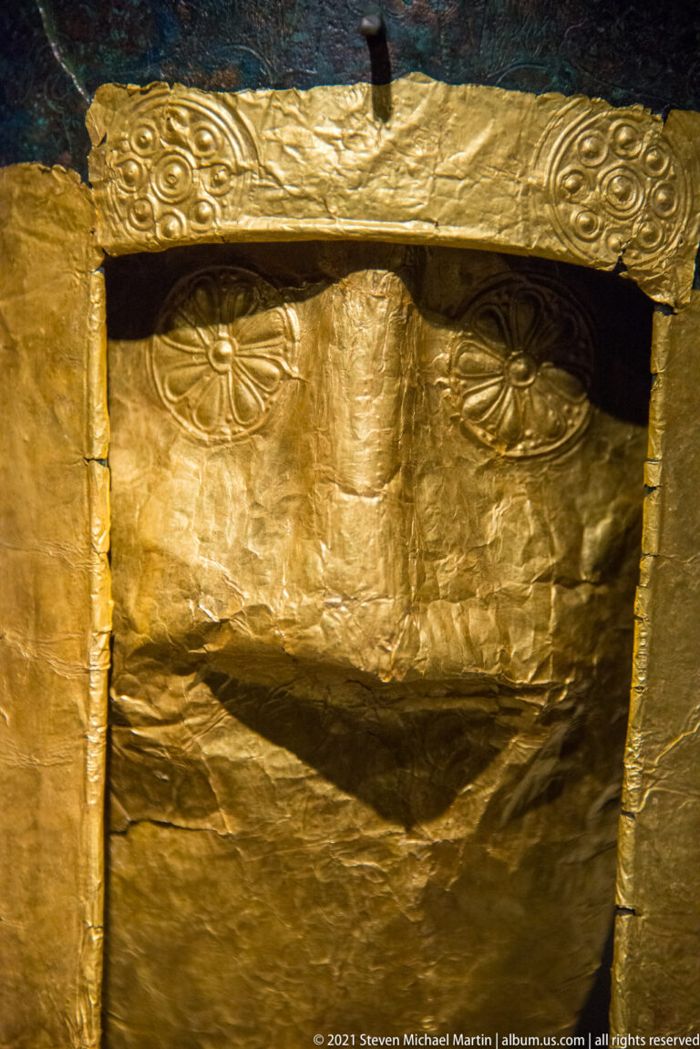 Close view of a wrinkled sheet-gold plate with embossed upper border attached to a bronze helmet opening.