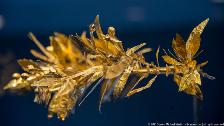 Delicate gold wreath made of thin branches with overlapping leaves, buds, and small blossoms.