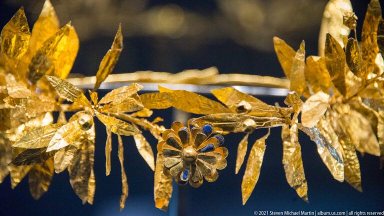 Close detail of a gold wreath with narrow leaves, a small rosette, and thin connecting stems.