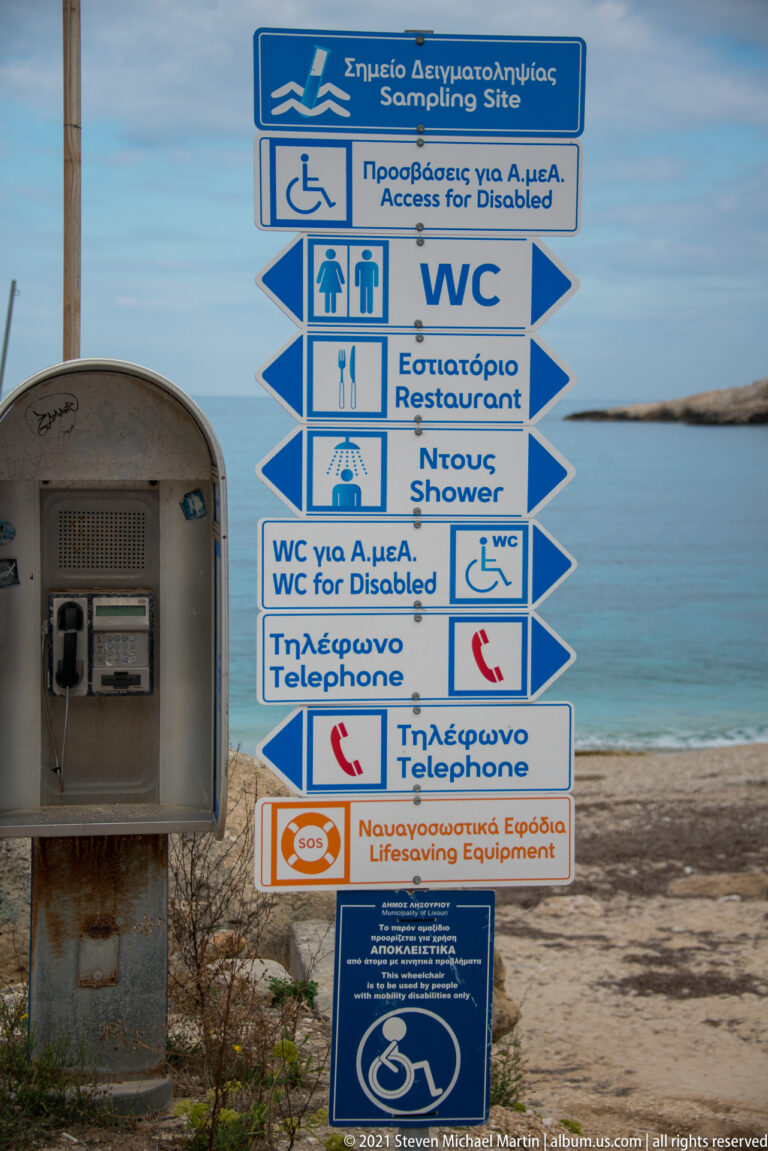Close view of bilingual beach-service signs for accessibility, toilets, restaurant, showers, telephones, and lifesaving equipment.