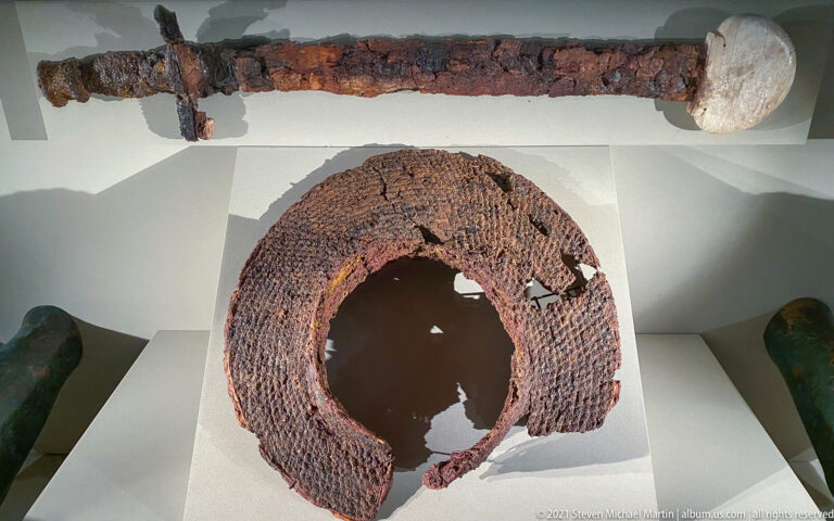 Two heavily corroded iron artifacts, including a long narrow piece with pale terminal and a large hollow curved fragment.