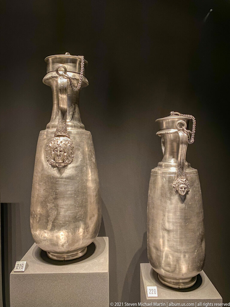 Two silver jugs of different sizes with rounded bodies, narrow necks, broad rims, and high decorated handles.