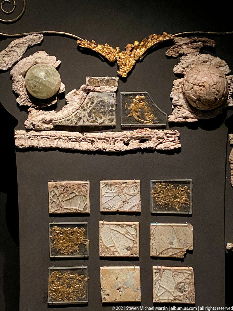 Assorted funerary furniture fragments including long carved strips, small plaques, gilded reliefs, pale inlays, and rounded elements.