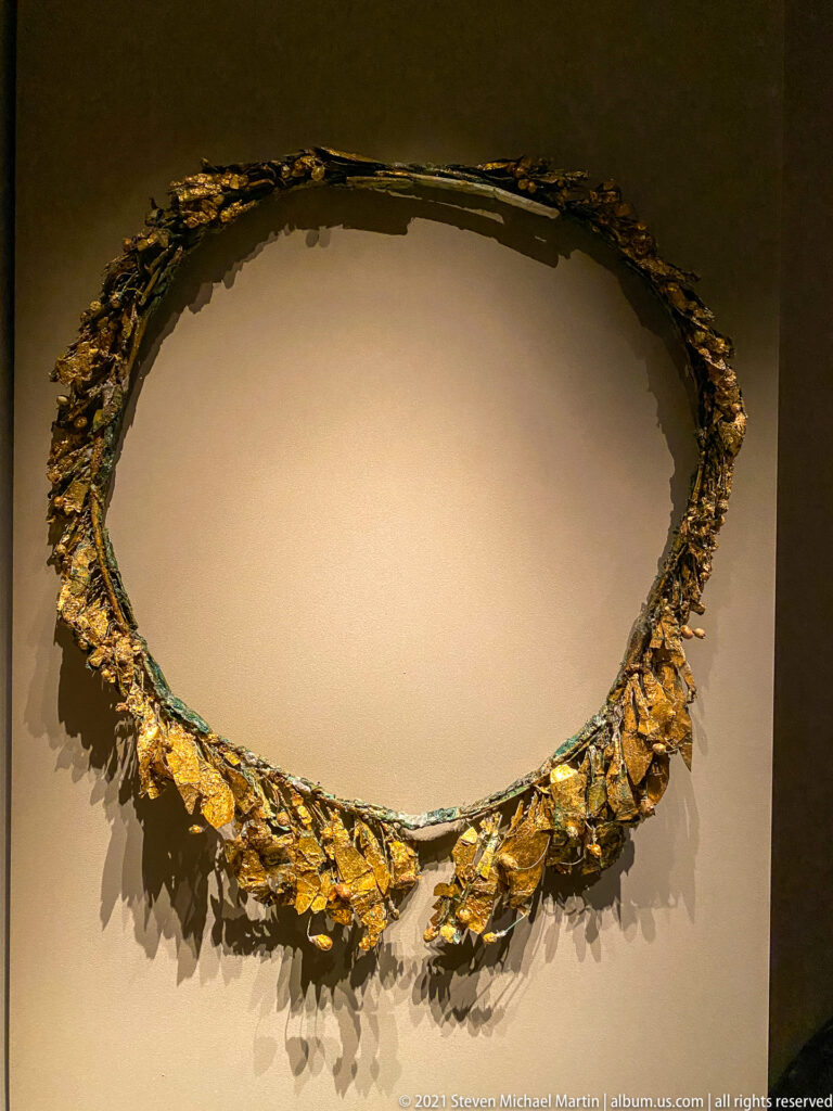 Fragmentary circular wreath with surviving gold leaves concentrated along the lower edge and a dark green-corroded supporting ring.