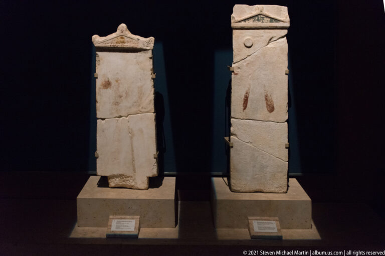 Two tall narrow stone grave markers with cracks and repairs; the right stele retains faint reddish painted marks.