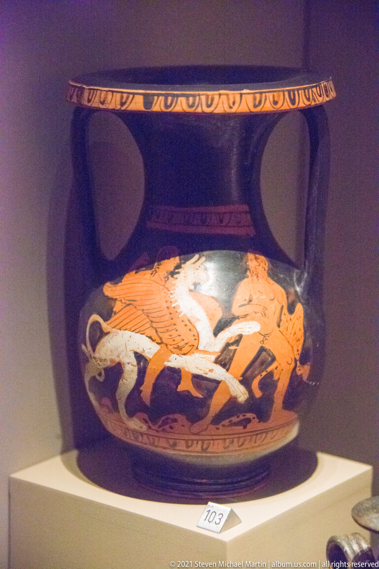 Black two-handled red-figure vessel with orange and white figures clustered around a horse on the body.