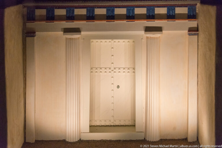Frontal view of a pale Macedonian tomb façade with central double door, flanking supports, and painted upper frieze.