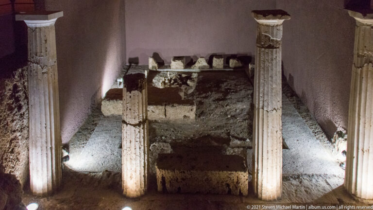 Illuminated ancient masonry and several slender columns preserved in situ inside the dark Royal Tombs museum.