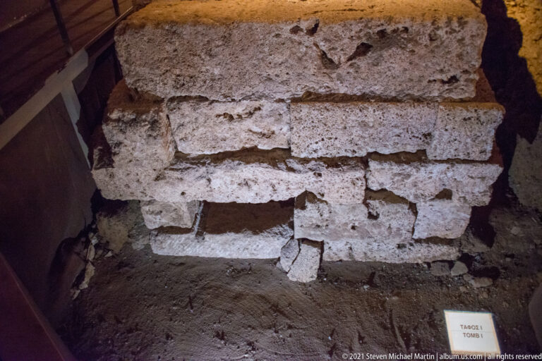Close view of rough pale block masonry in the excavated area, with a small label identifying Tomb I.