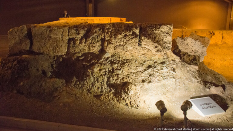 Spotlit ancient masonry blocks and rough wall fabric preserved in the excavated Heroön area at Aigai.