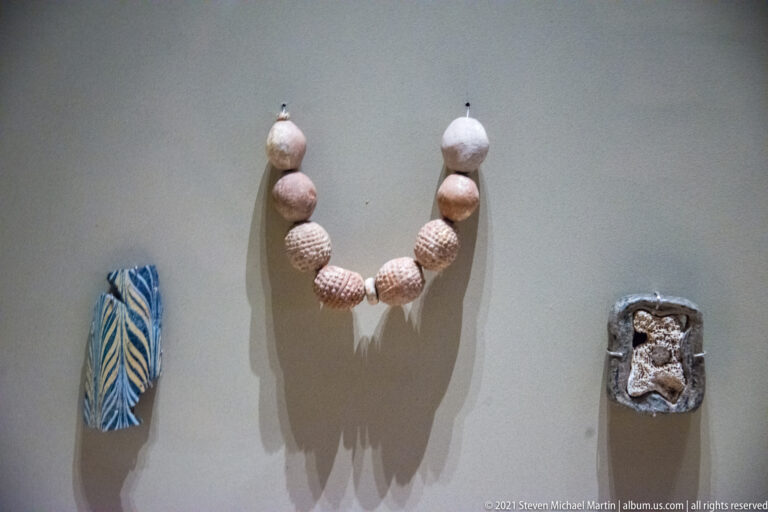 Strand of spherical beads displayed between a blue-and-white leaf-shaped ornament and a small dark rectangular fitting.