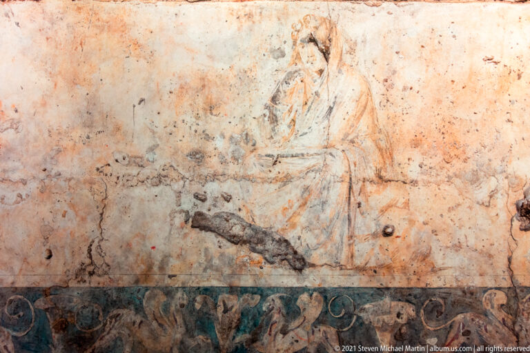 Faded seated draped figure above a dark painted border of scrolling vegetal ornament.