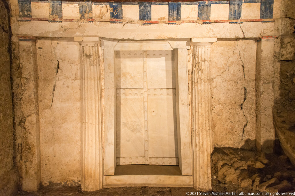 Close frontal view of the Tomb of Philip II’s marble double doors framed by Doric architectural elements and painted bands.
