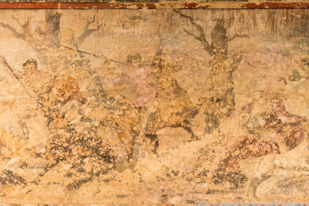 Weathered ancient plaster with faint brown and reddish figural outlines surviving across a mottled ocher surface.