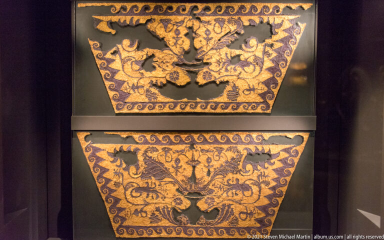 Two trapezoidal purple textile fragments covered with symmetrical gold vegetal scrolls, palmettes, and small decorative motifs.
