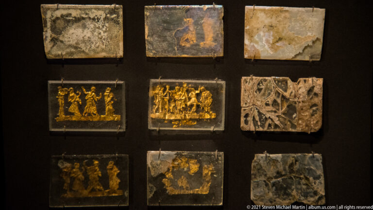 Nine square and rectangular couch plaques in a grid, several with gilded figures and others with pale carved or faded decoration.