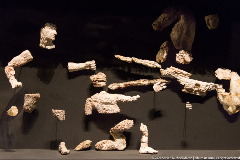 Scattered carved ivory hands, arms, legs, feet, and torso fragments mounted individually against a black background.