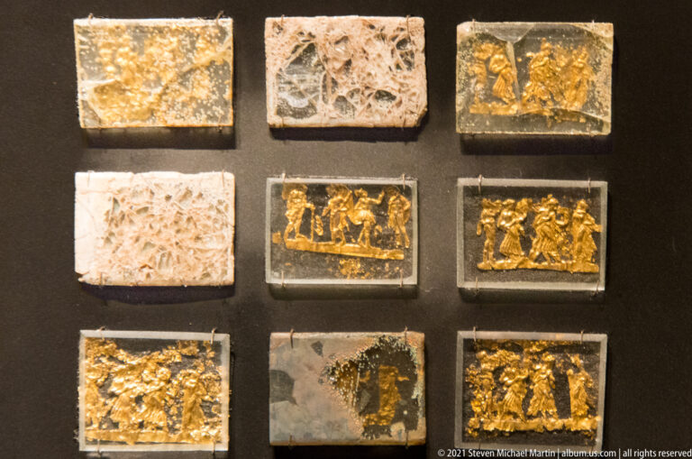 Nine fragmentary decorative plaques arranged in rows, including gilded figure scenes, pale carved panels, and dark damaged pieces.