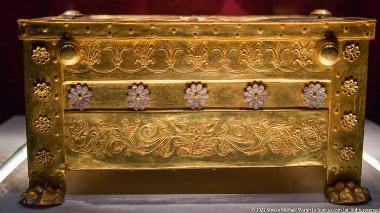 Oblique view of the gold larnax from the Tomb of Philip II showing lion-paw feet, rosettes, and embossed borders.