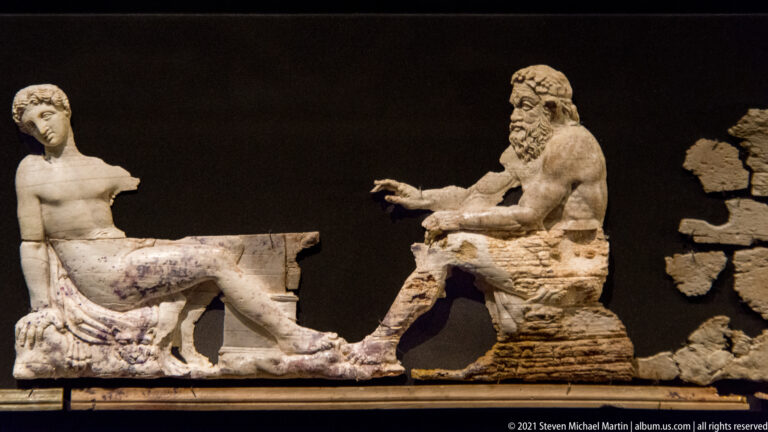 Large ivory group with a youthful reclining male figure at left and an older bearded seated male figure at right.