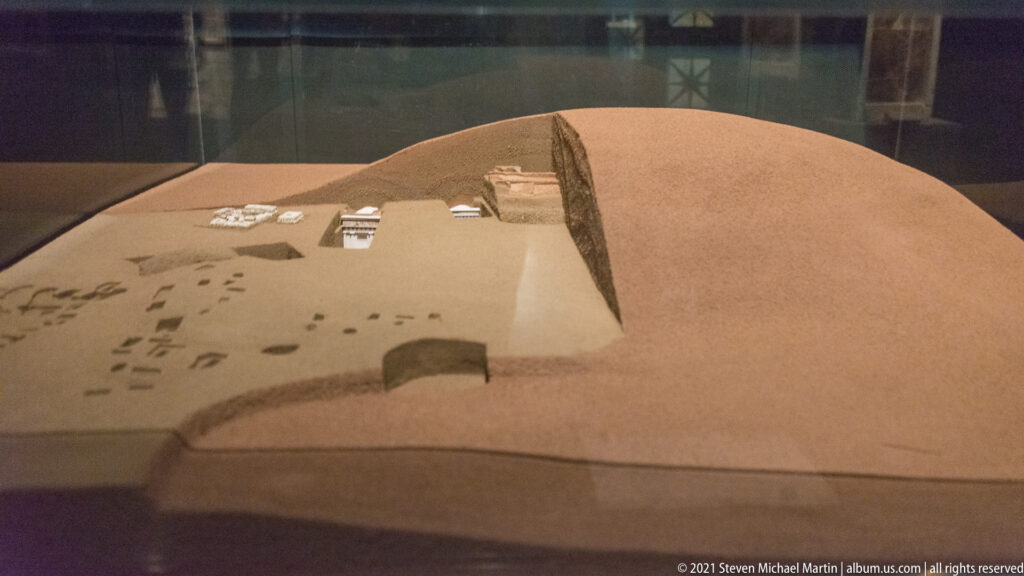 Museum model showing a cutaway earthen tumulus with tomb structures and smaller burial features beneath its surface.