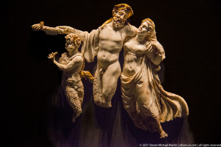 Three carved ivory figures from the Prince’s Tomb funerary couch, centered on a muscular bearded male with an outstretched arm.
