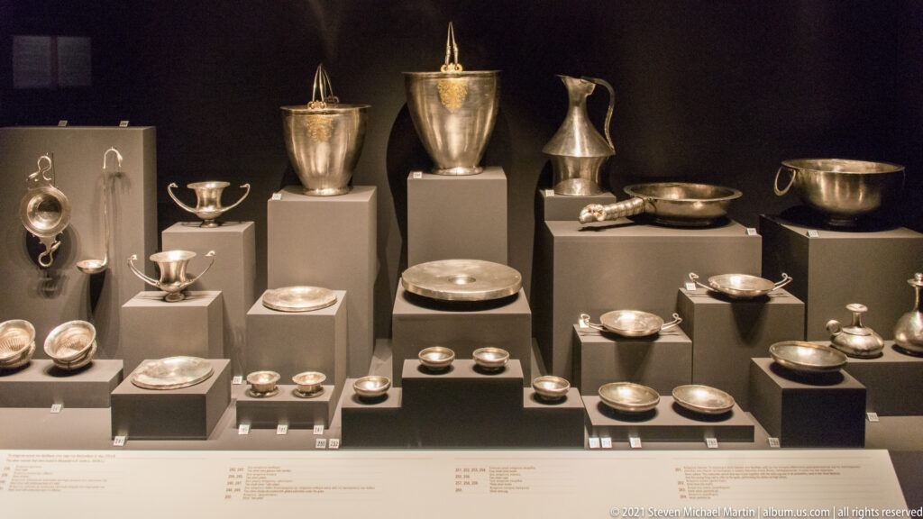 Museum display of silver cups, bowls, plates, jugs, and lidded vessels from Tomb III, the Prince’s Tomb.