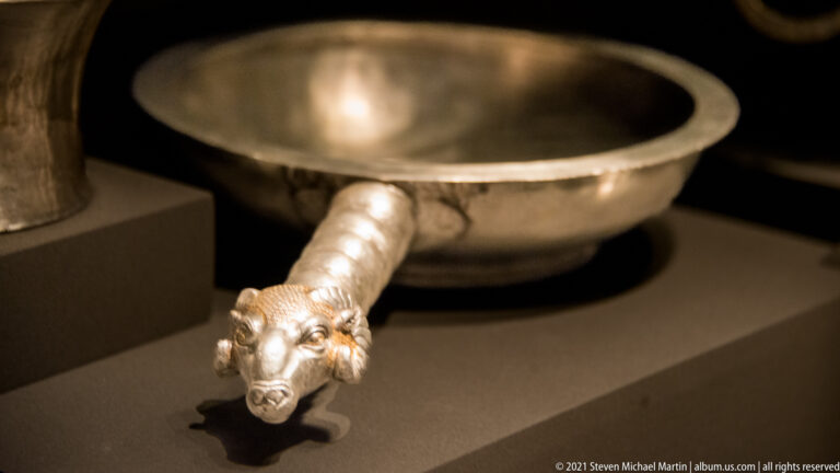 Shallow silver pan with a projecting handle ending in a finely modeled horned animal head.