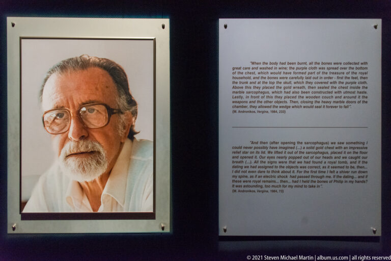 Formal portrait of an elderly bearded man with glasses and a white shirt, identified in the museum context as Manolis Andronikos.