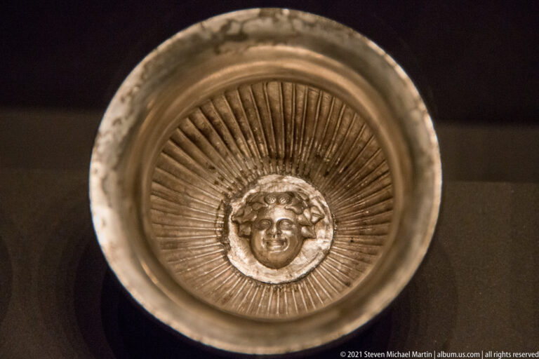 Silver bowl with radiating flutes and a round curly-haired face medallion centered inside the vessel.