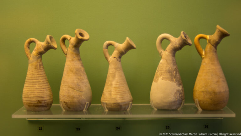 Five small ceramic jugs with narrow necks, loop handles, and elongated bodies arranged side by side.