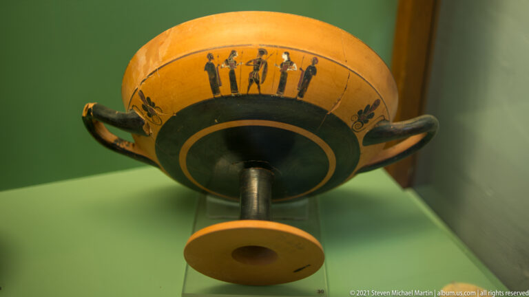 Shallow two-handled stemmed cup viewed from below, with a black underside and small painted figure band near the rim.