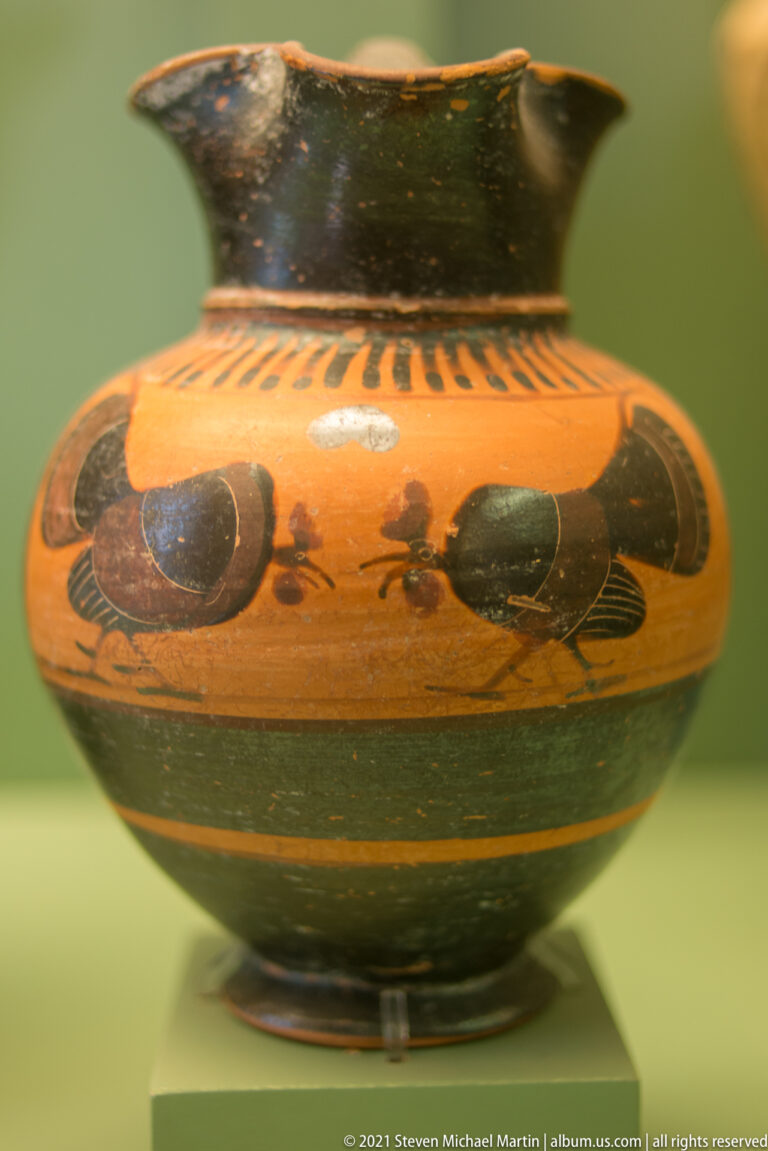 Squat ceramic vessel with repeated dark animal silhouettes, a broad black lower zone, and radiating neck ornament.