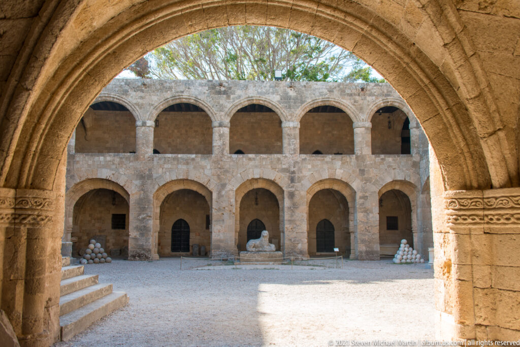Broad pointed arch opening onto a sunlit courtyard surrounded by two levels of stone arcades.