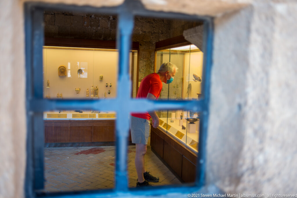 Visitor in a red top examining illuminated display cases, viewed through a deep stone opening inside the museum.