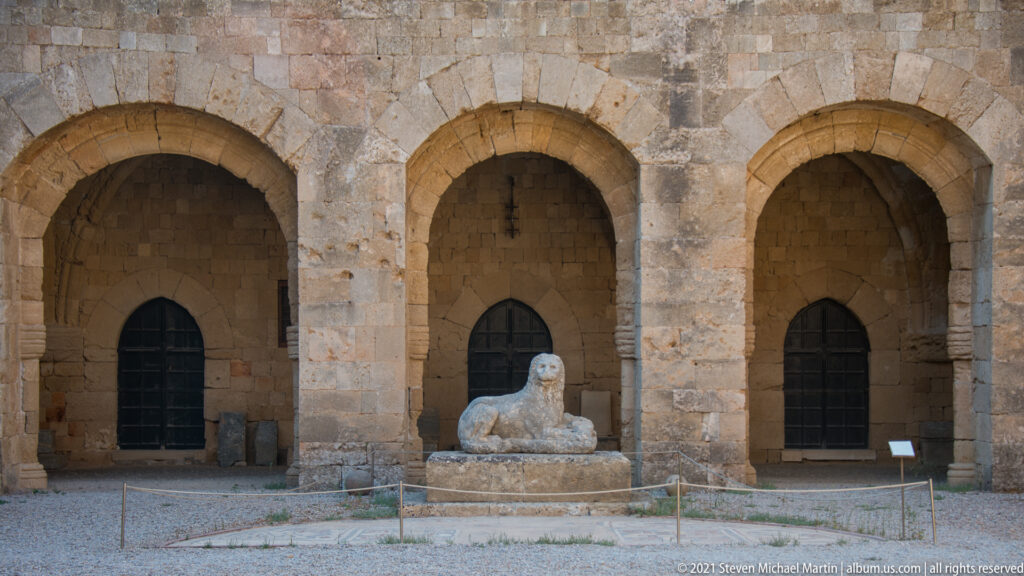 Reclining stone lion on a low plinth before three arched recesses in the museum courtyard.