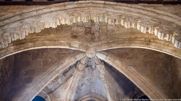 Upward view of a stone rib vault with radiating ribs, central boss, and carved molding.