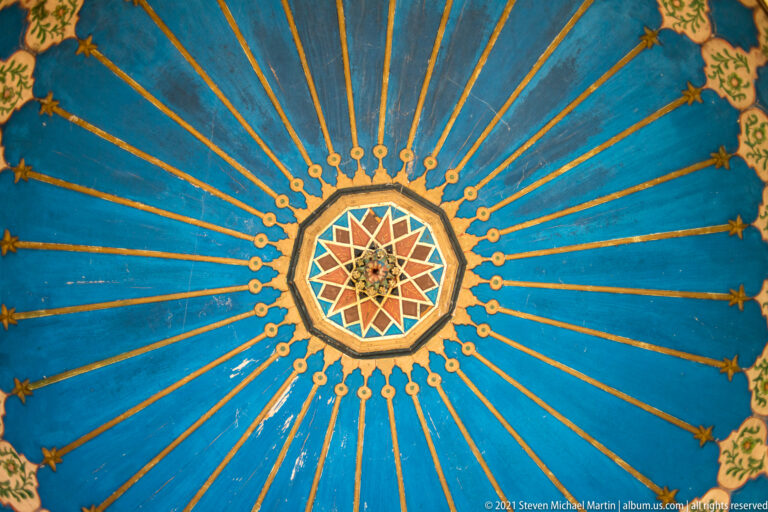 Blue painted ceiling with gold radial lines centered on a multicolored geometric star rosette.