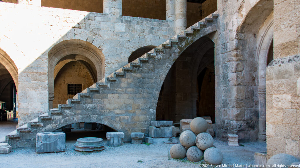Diagonal stone staircase above an arch, with carved fragments and large stone spheres arranged at ground level.
