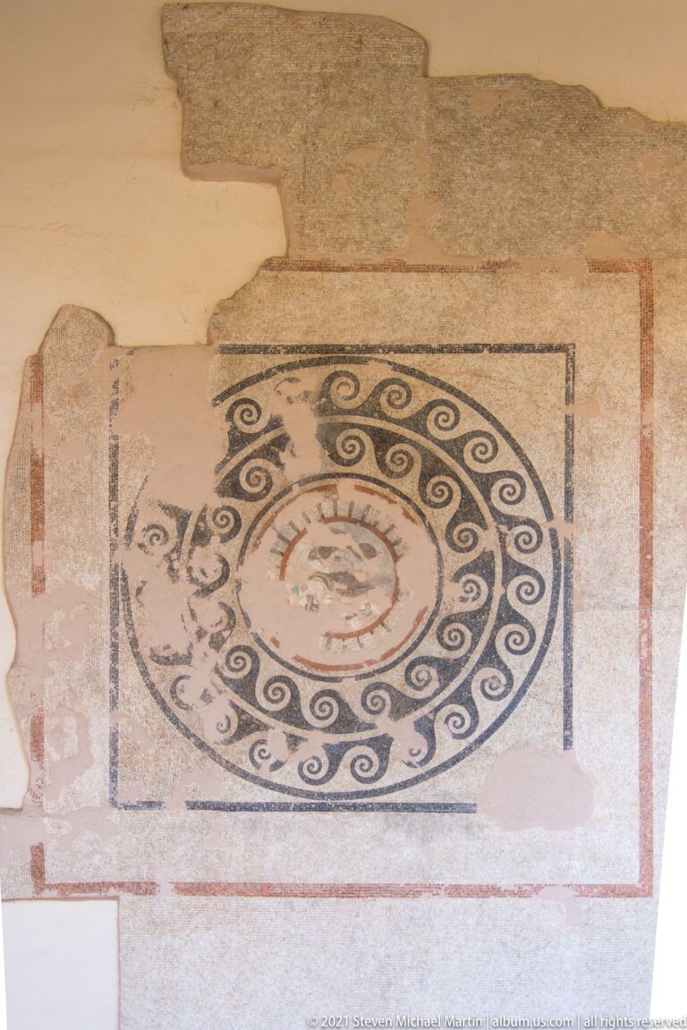 Fragmentary mosaic with concentric circular bands of dark spirals around a small central medallion.