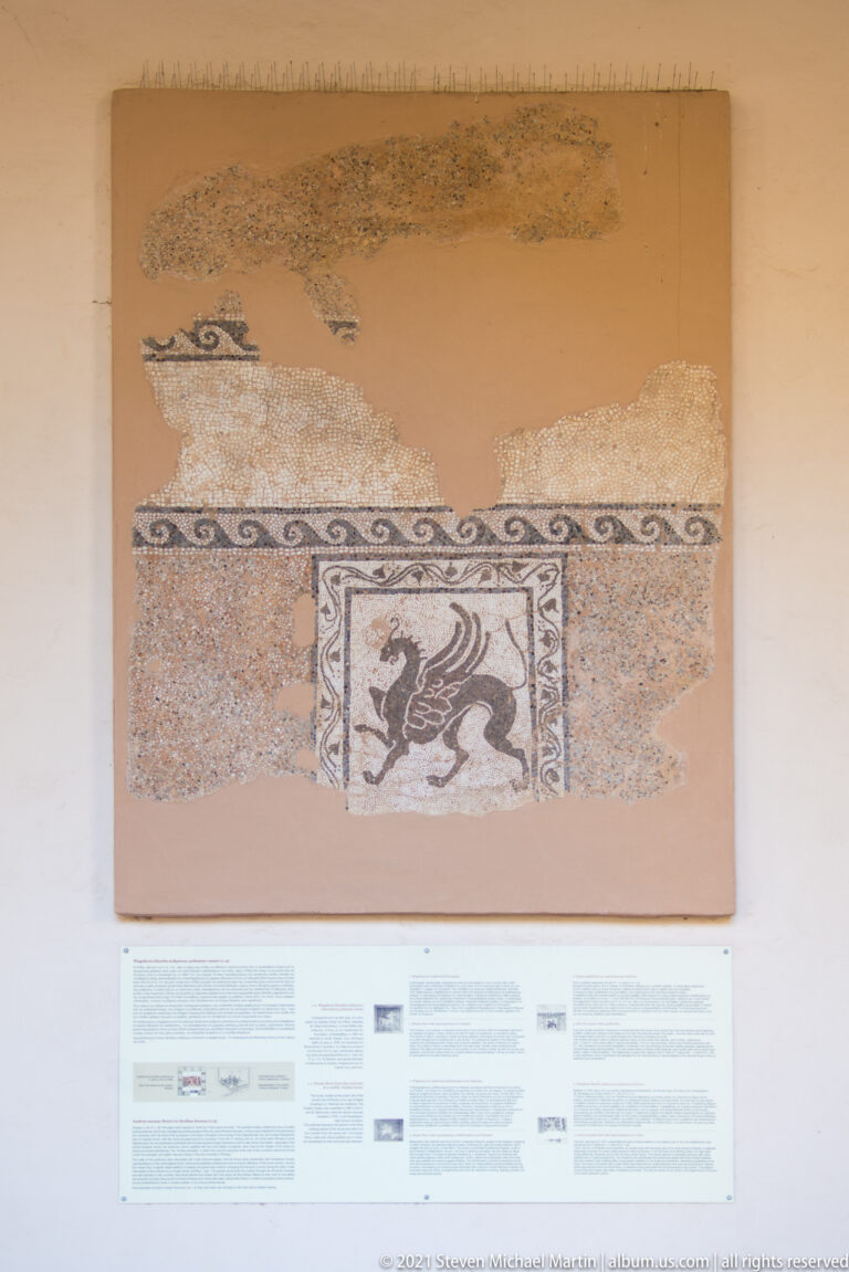 Mounted fragmentary mosaic with a small framed panel containing a dark animal figure.