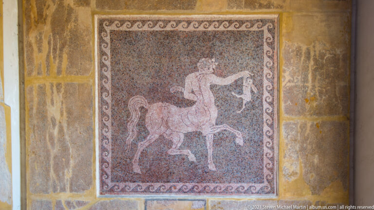 Rectangular mosaic panel showing a rider on horseback within a narrow scrolling border.