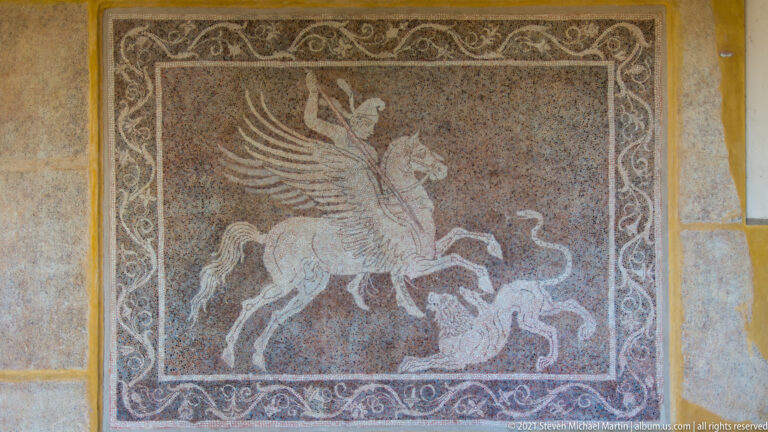 Mosaic showing a rearing winged horse with two human figures inside a scrolling vegetal border.