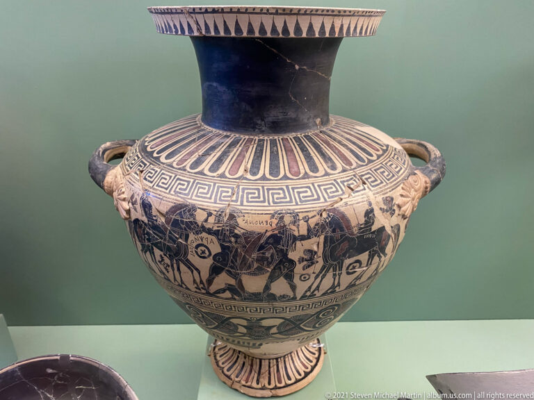 Large two-handled black-figure vessel with tall neck, narrative frieze, horses, figures, and geometric border bands.