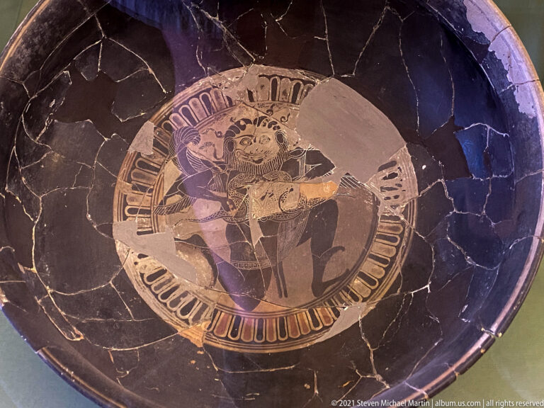 Overhead view inside a reconstructed dark-glazed bowl with a central painted figural medallion and visible repair joins.