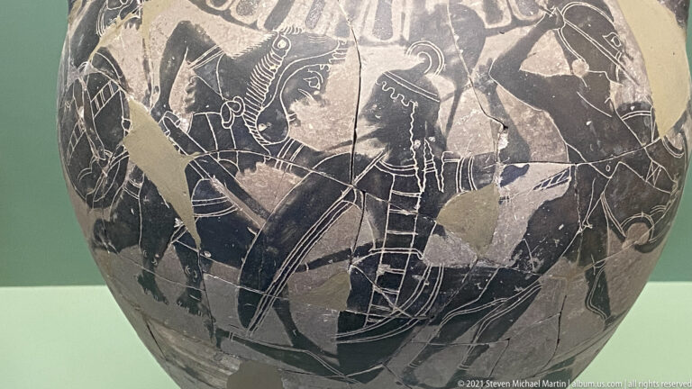 Fragmentary black-figure vase scene with overlapping armed warriors, shields, helmets, and spears.