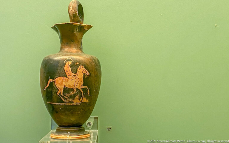 Tall dark-glazed jug with a reserved red-figure panel showing a rider on horseback.