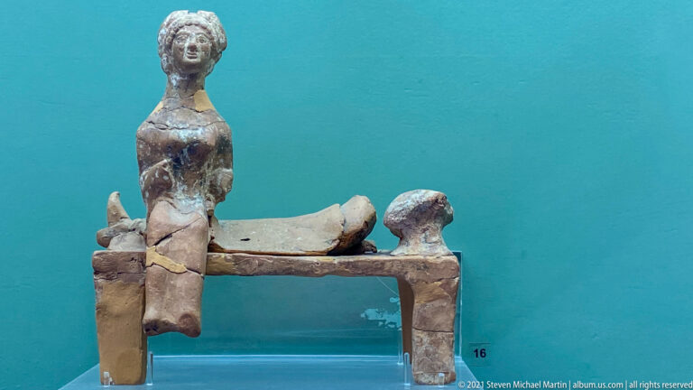 Fragmentary terracotta model with four legs, raised corner figures, and a curved piece resting across the top.