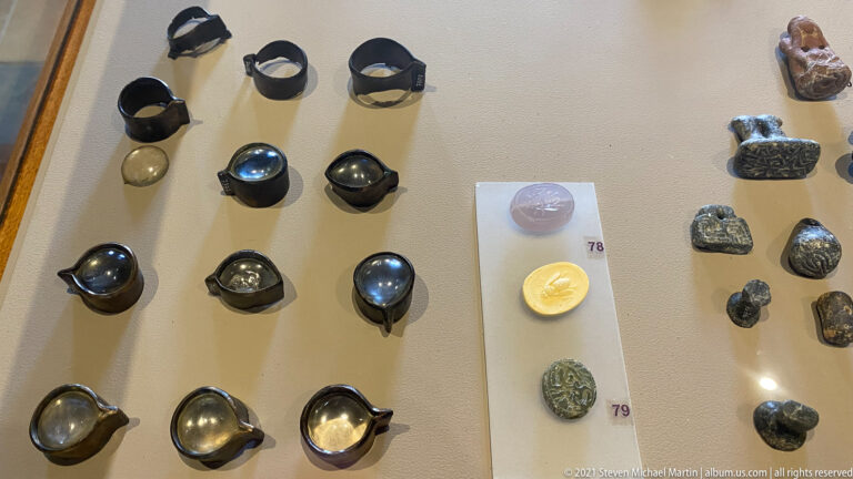 Display case containing dark rings, polished stones, seals, beads, and other small numbered personal objects.